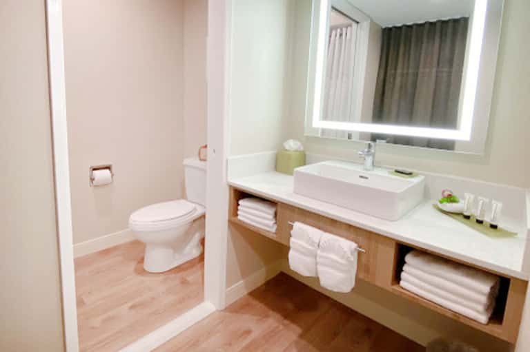 Modern hotel bathroom with white vessel sink, illuminated mirror, and wooden vanity storage