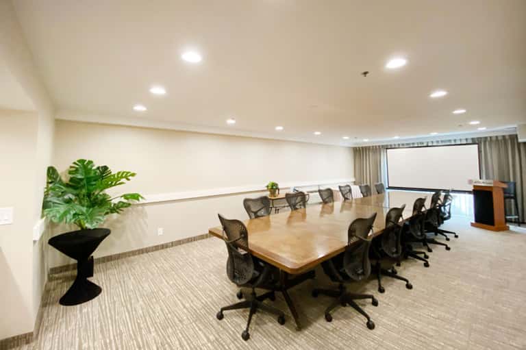 Modern conference room with long wooden table, mesh chairs, and projection screen
