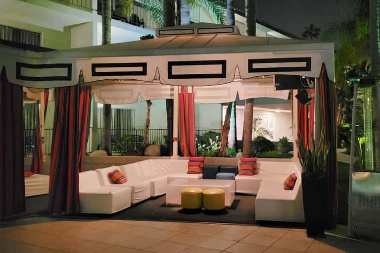Modern lounge cabana with pink seating, red curtains, and geometric black design elements