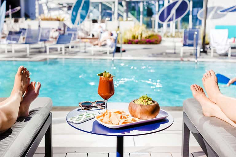 Poolside dining table with cocktail and appetizers overlooking sparkling resort swimming pool