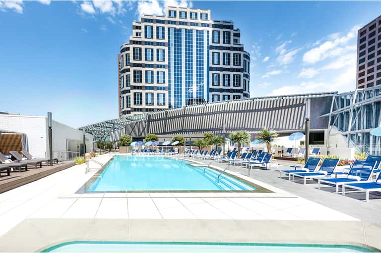 Modern rooftop pool with blue loungers, architectural overhang and tall residential building backdrop
