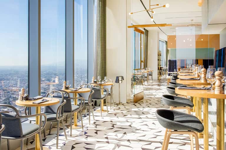 Fine dining restaurant with floor-to-ceiling windows overlooking cityscape and modern table settings