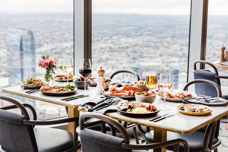 Fine dining table with multiple courses and city skyline view from high-rise restaurant