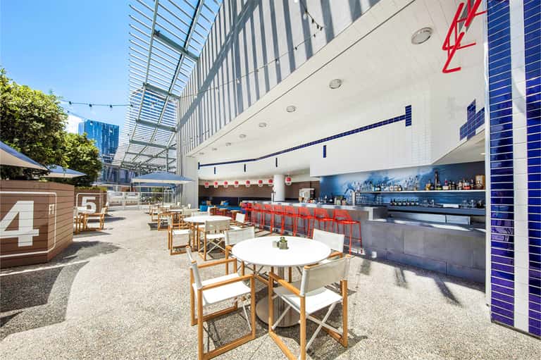Outdoor poolside bar and lounge area with red seating, numbered wooden structures, and contemporary design