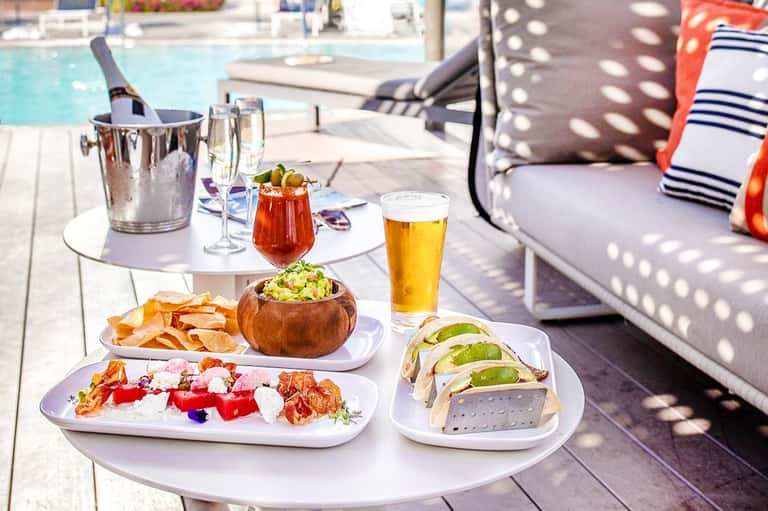 Poolside table with appetizers, cocktails, champagne bucket, and lounge seating overlooking swimming pool