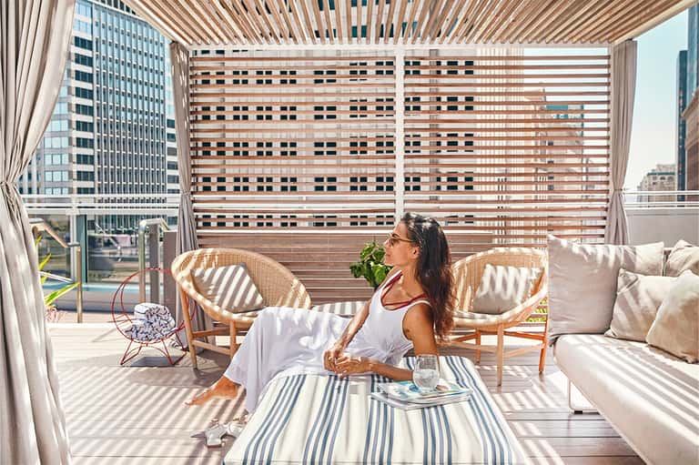 Woman relaxing on sunny rooftop terrace with striped shade screen and city views