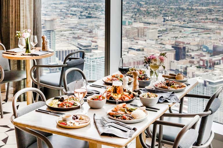 Fine dining table set high above cityscape with plated dishes, flowers, and wine glasses