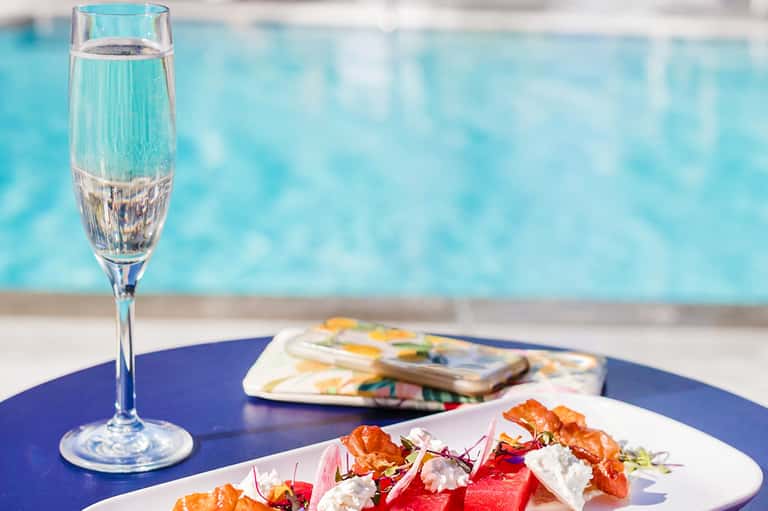 Plated appetizers and champagne glass by the pool overlooking blue water