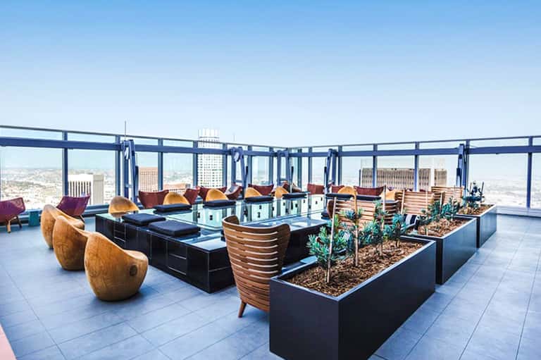 High-rise rooftop lounge with wooden chairs, planters, and panoramic city skyline views