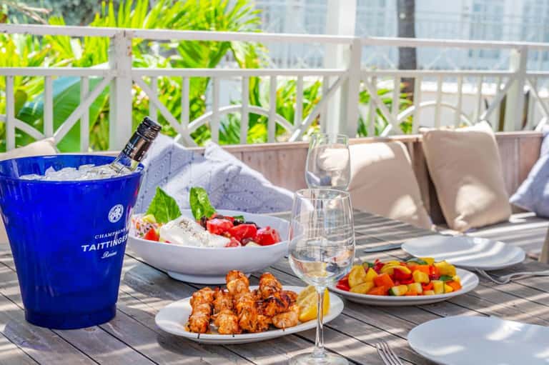 Luxury resort balcony table with champagne bucket, gourmet dishes, and city skyline view beyond railing