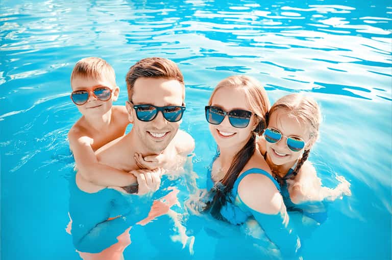 Family of four enjoying indoor swimming pool, smiling and wearing colorful sunglasses
