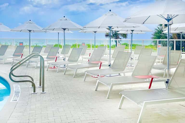 Oceanfront pool deck with white lounge chairs and umbrellas overlooking the beach and sea
