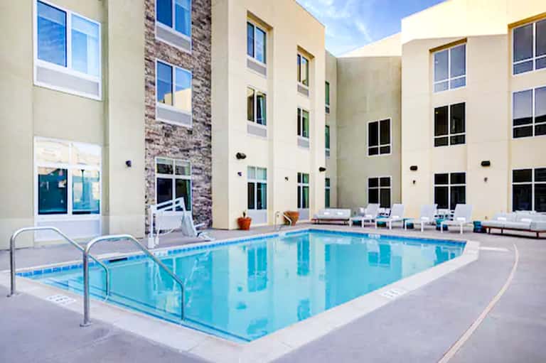 Indoor hotel pool with metal railings, white loungers, and modern building architecture
