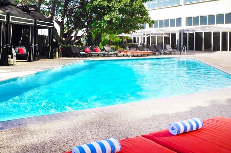Contemporary hotel pool with turquoise water, lounge chairs, black cabanas, and modern building