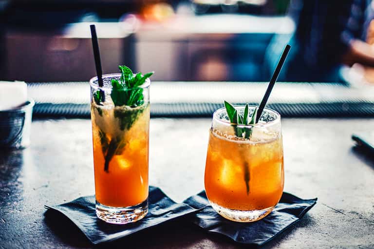 Two tropical cocktails with mint garnish and black straws on slate coasters