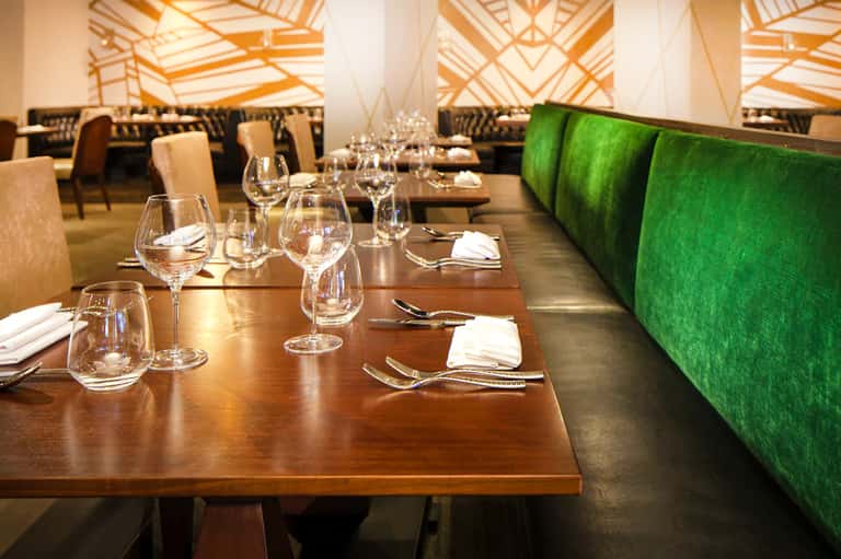 Fine dining restaurant with wooden tables, wine glasses, and geometric ceiling design