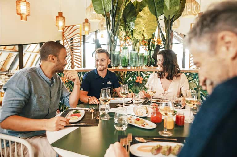 Group dining at tropical restaurant with botanical decor, hanging lanterns, and lush plant surroundings