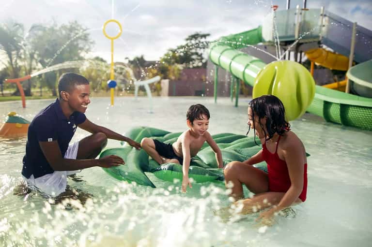 Family playing together in shallow resort pool with inflatable raft and splash pad equipment