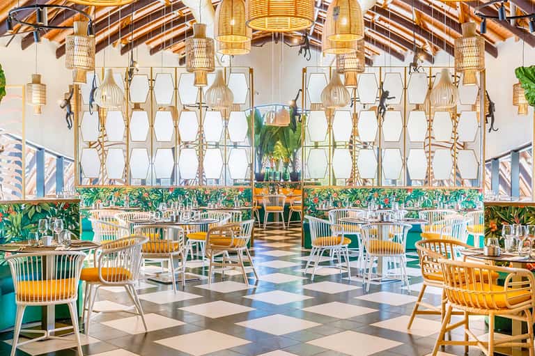 Upscale restaurant interior with woven pendant lights, tropical plants, and checkered floor