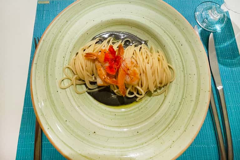Spaghetti with whole fish and tomatoes in green sauce on a light green plate