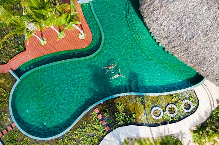 Aerial view of turquoise lagoon-style pool with swimmers and red wooden deck