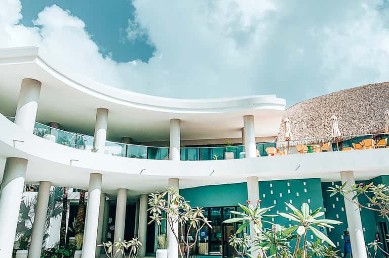 Contemporary curved white building with columns overlooking beachfront resort area