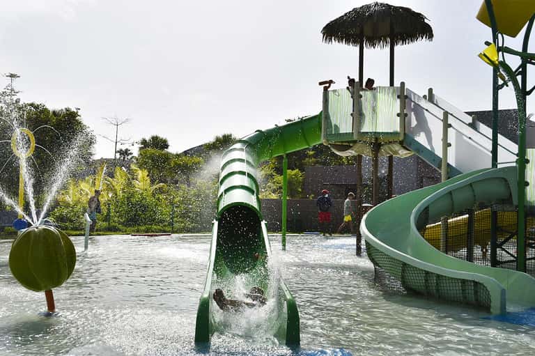 Water play area with green slide, splash features, and palm trees