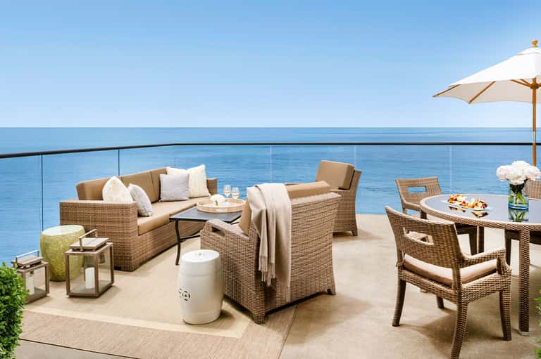 Oceanfront terrace with wicker furniture, umbrella, and coastal seating area