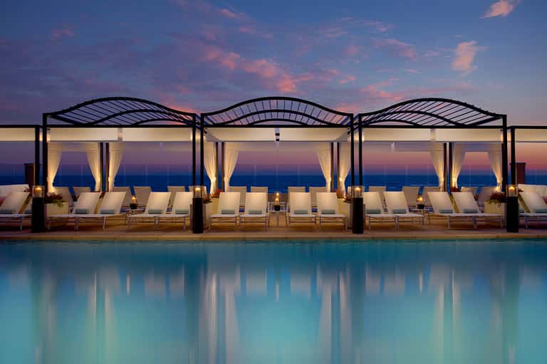 Luxury poolside cabanas with white curtains at sunset overlooking the ocean