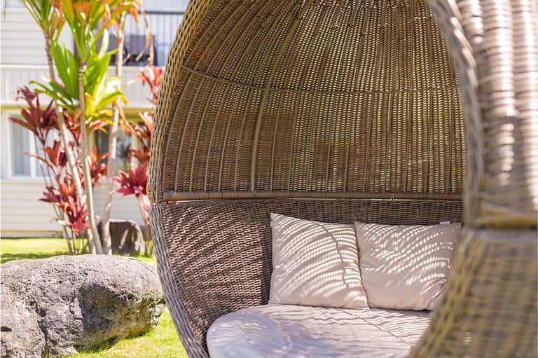 Woven rattan hanging chair with cushions and tropical red flowers in natural outdoor setting