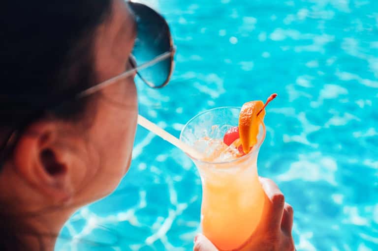 Person enjoying tropical cocktail by the pool wearing sunglasses