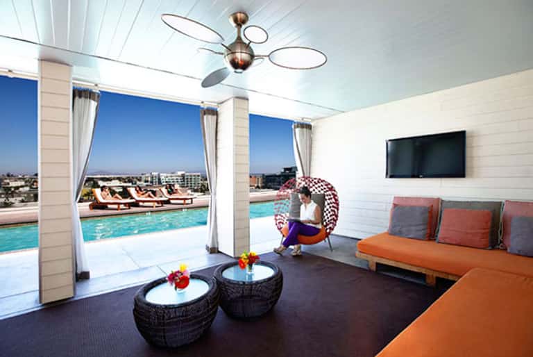 Modern rooftop lounge with orange seating, ceiling fan, and panoramic city pool views through floor-to-ceiling windows