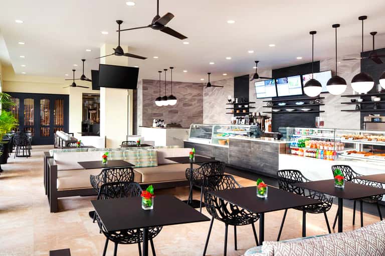 Modern hotel cafe and lounge with black pendant lights, marble walls, black chairs, counter seating, and contemporary design