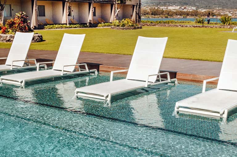 Resort pool with white loungers partially submerged, green lawn, and mountain lake views