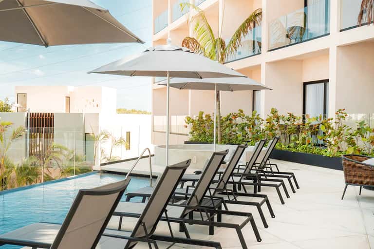 Resort poolside with gray umbrellas, black lounge chairs, and modern building with palm trees