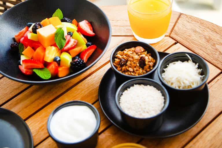 Healthy breakfast bowl with fresh fruit and juice, plus yogurt and granola toppings on wooden table