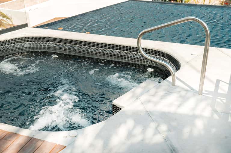 Outdoor spa hot tub with black mosaic tiles next to a larger swimming pool