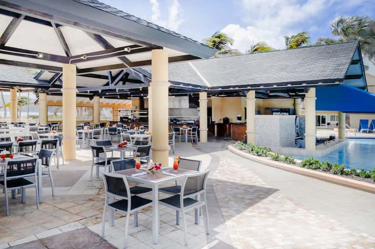 Beachfront dining area with white tables, black chairs, and covered pavilion overlooking ocean