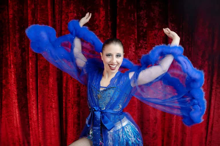 Performer in blue sequined costume with flowing fabric against red velvet curtain backdrop