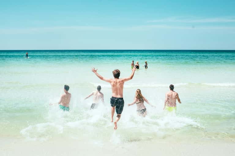 Group of children and young people running into bright turquoise ocean water on a sunny beach day