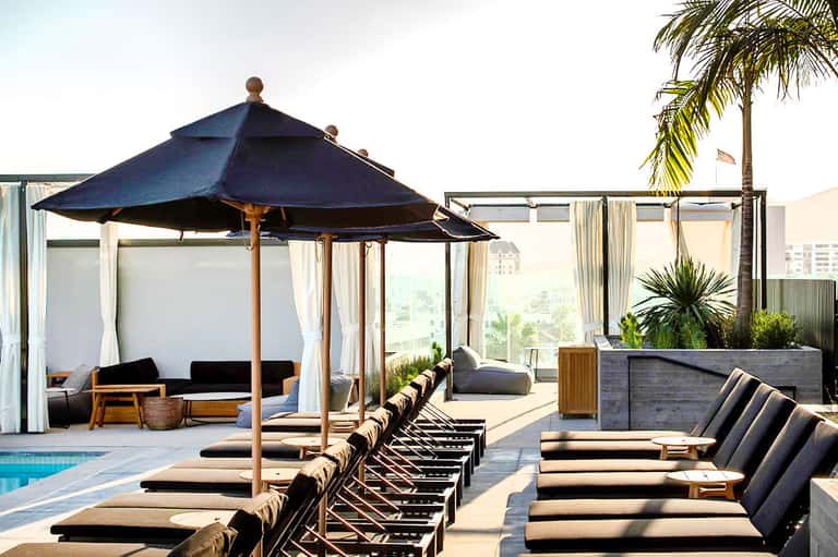 Modern rooftop pool deck with lounge chairs, blue umbrella, and city skyline views