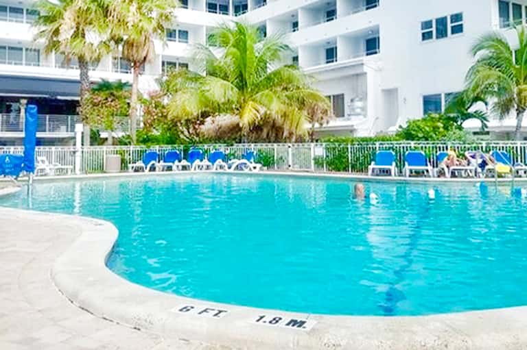 Large resort pool with depth markers, surrounded by blue lounge chairs and palm trees