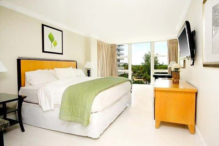 Hotel bedroom with orange headboard, green throw blanket, and balcony view of tropical landscape