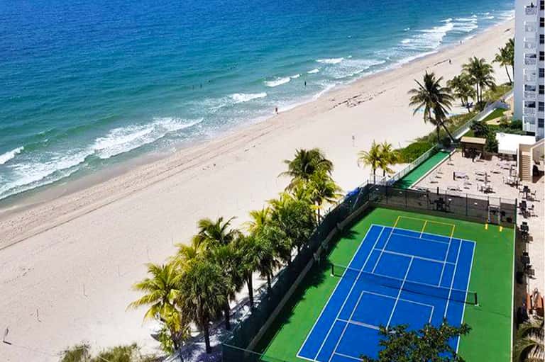 Beachfront property with tennis court, ocean view, and white high-rise building