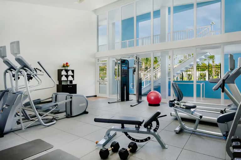 Fitness center with exercise equipment and floor-to-ceiling windows overlooking a pool and palm trees