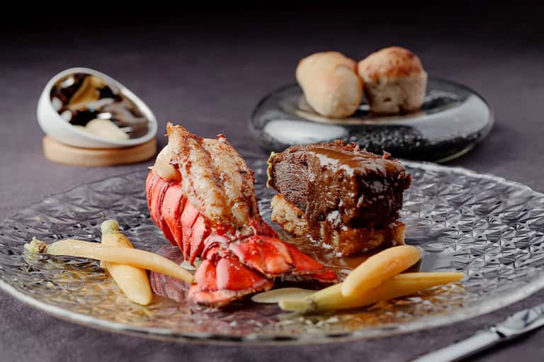 Gourmet plated seafood dish featuring lobster tail and seared protein on dark slate plate