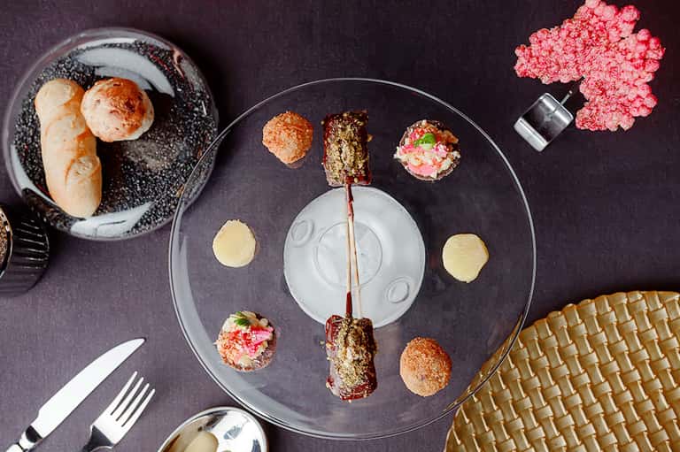 Gourmet plated appetizers on black dinnerware with bread and pink garnish