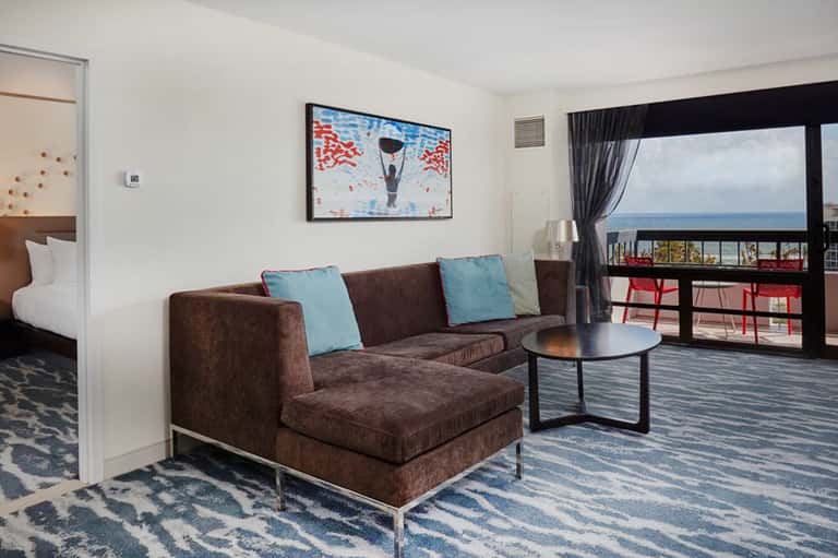 Hotel suite with brown sectional sofa, ocean view balcony, and contemporary furnishings