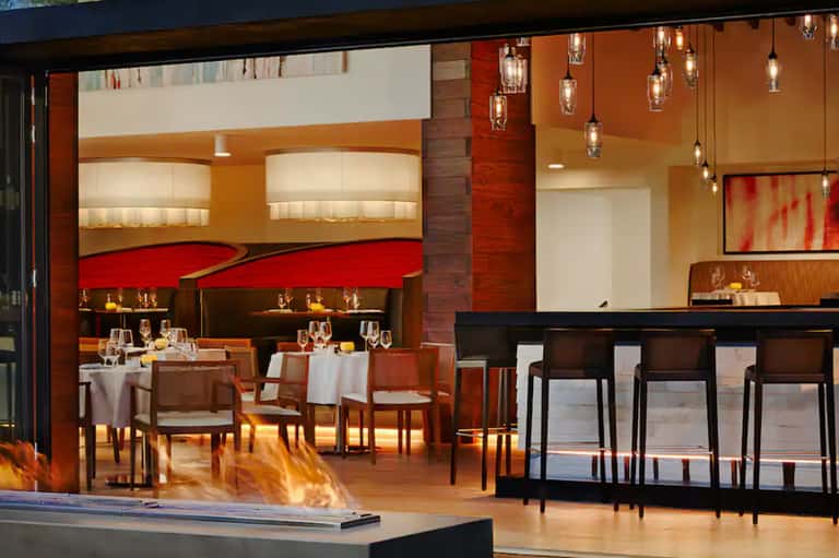 Contemporary fine dining restaurant with red and orange accents, hanging glass pendant lights, and open kitchen