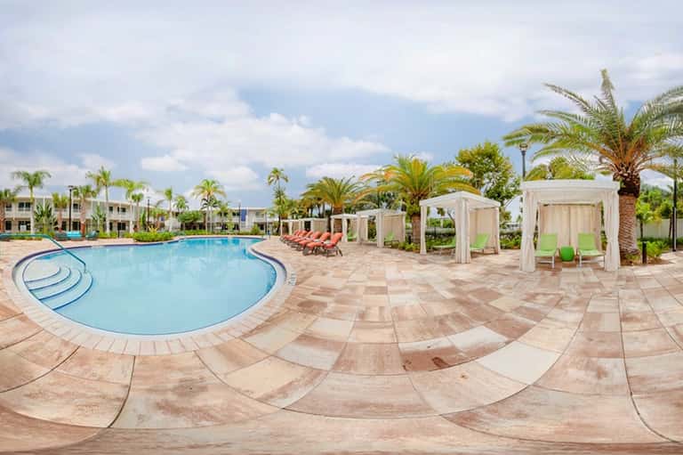 Resort pool with curved design, white cabanas, palm trees, and lounge seating